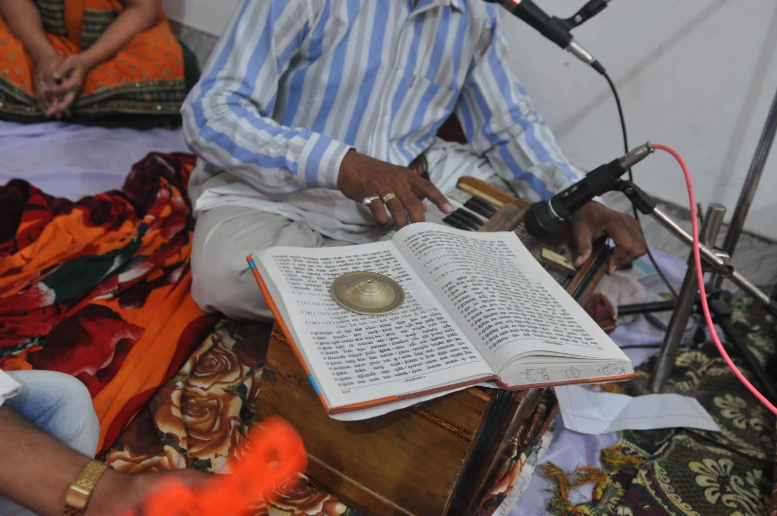 Close view of an open book above the harmonium, beside a microphone and the musician’s hands.