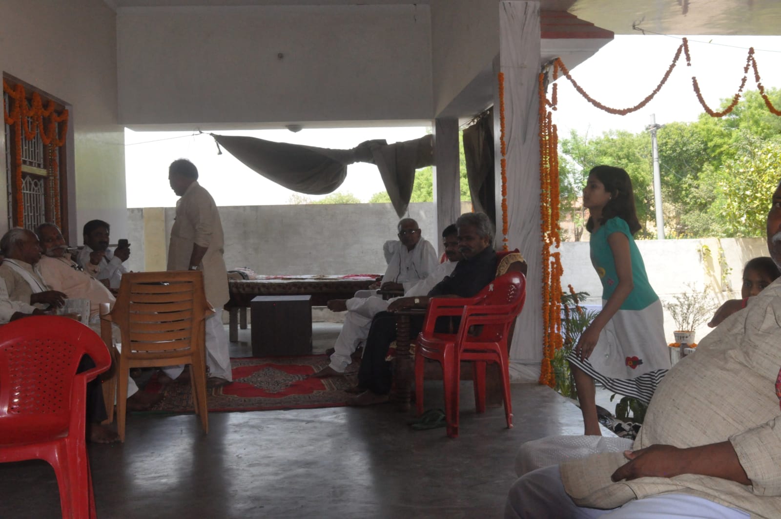 People seated on chairs and on the floor in an open room, with a girl standing near the doorway.