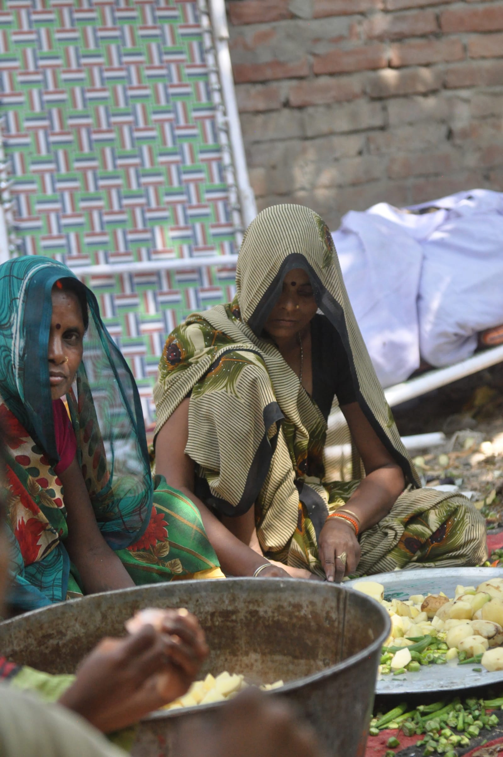 Two women seated beside bowls and vegetables in the food-preparation area.