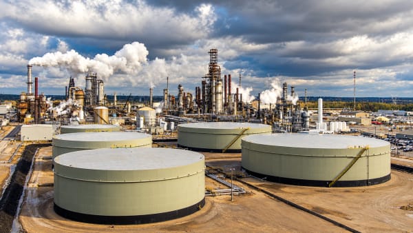 Aerial view of a refinery and its crude storage tanks under heavy cloud, with steam rising from the process units