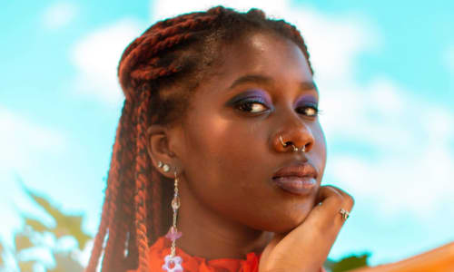 Kara Jackson is a black woman who is wearing a bright orange long sleeved top. 