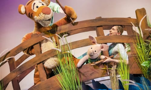 Puppets of Tigger and Piglet on a bridge on stage playing pooh sticks