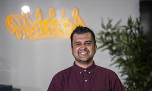Safyan is wearing a maroon coloured shirt and smiling at the camera.