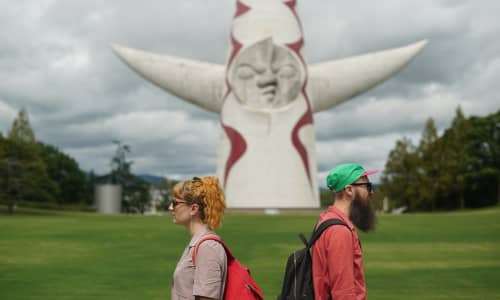 A woman back to back with a man wearing a green baseball hat, with a large sculpture in the background