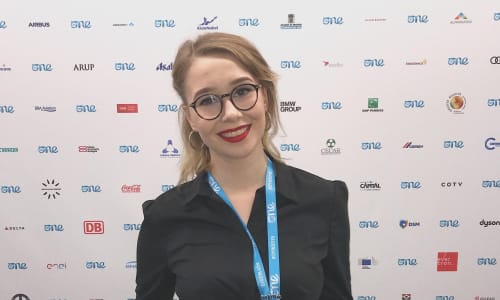 A young woman wearing white checked trousers and a black shirt is smiling