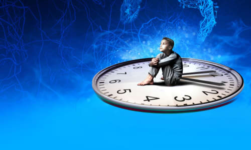 A young boy in pyjamas sat on a giant clock face looking upwards