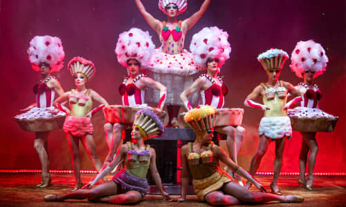 Drag queens on stage against a red backdrop