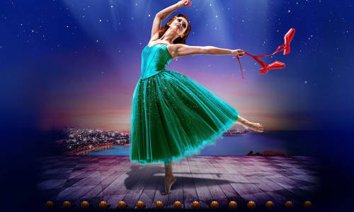 Ballerina in green dress dancing under the spotlight with a pair of red shoes in her hand.