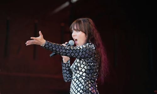 Singer wearing a sparkly outfit with her arm outstretched