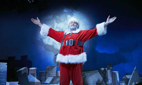 Father Christmas in his red and white clothes, stood in front of a dark blue background.