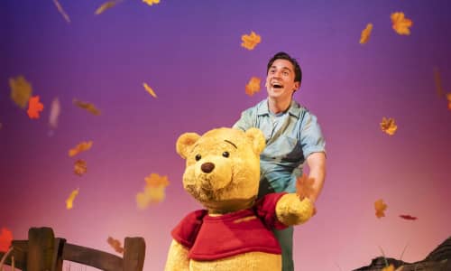 Winnie the Pooh ar y llwyfan gyda dail hydrefol yn syrthio o'i amgylch a'i bypedwr tu ôl iddo