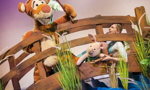 Puppets of Tigger and Piglet on a bridge on stage playing pooh sticks