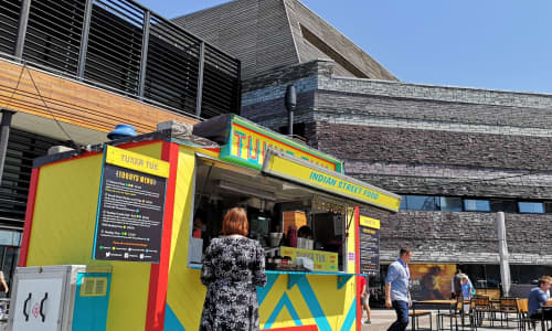 A woman standing next to a pop up street food vendor