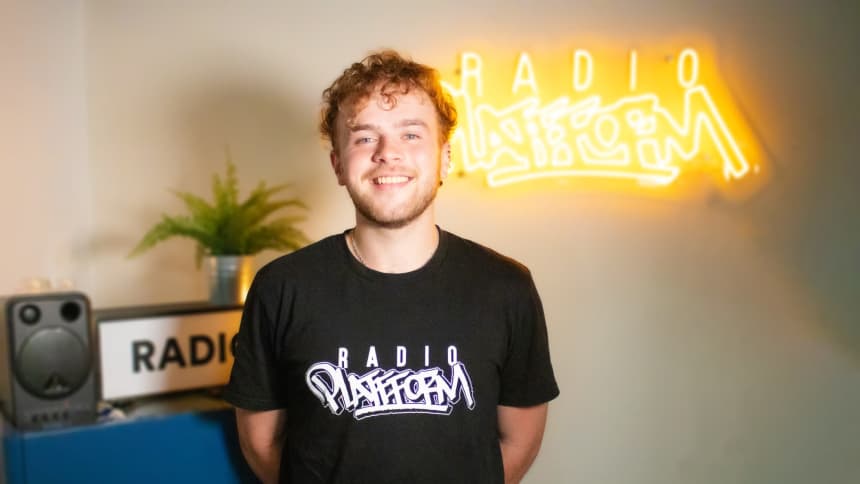 Rhys has short, wavy brown hair and is wearing a black Radio Platfform t-shirt.