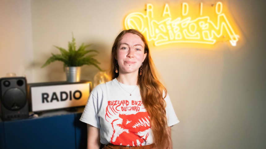 Zu has long brown hair and she is wearing a Buzzard Buzzard Buzzard band t-shirt.