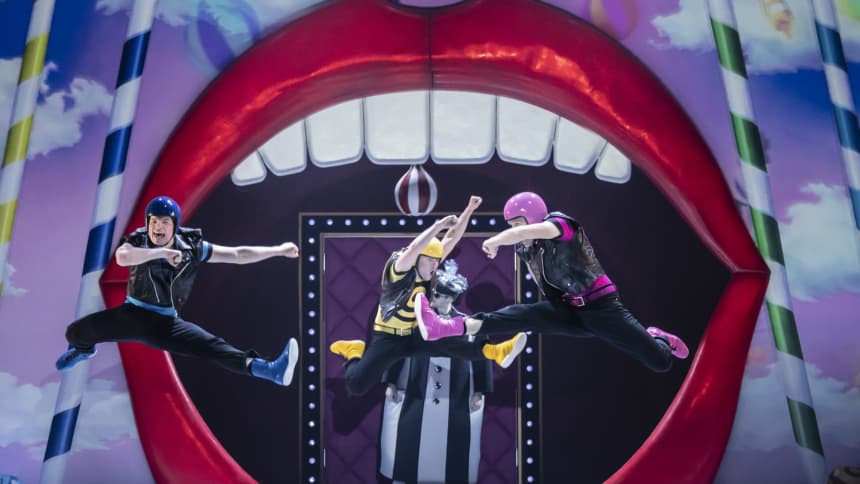 3 Dancers with coloured helmets leaping in front of a giant pair of lips and teeth 