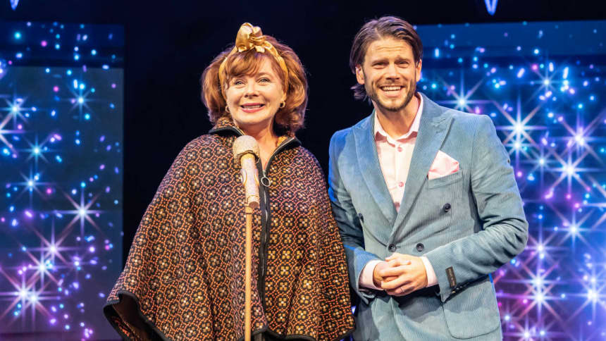 A woman on stage with a gold microphone stood next to a TV presenter