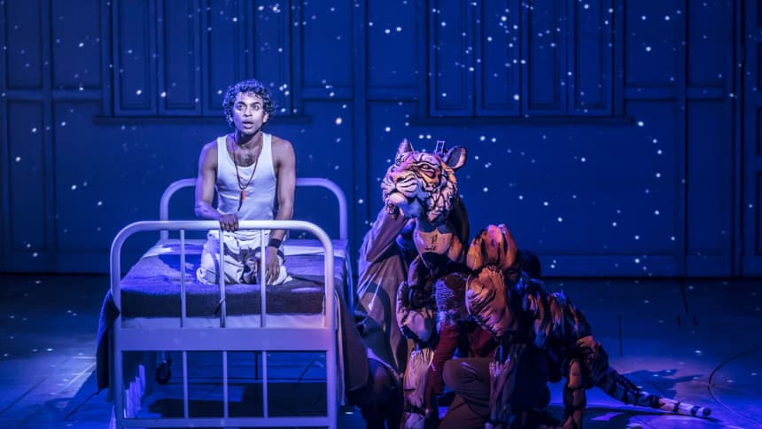 A young Indian boy kneeling on a hospital bed with a puppet tiger next to him on the floor