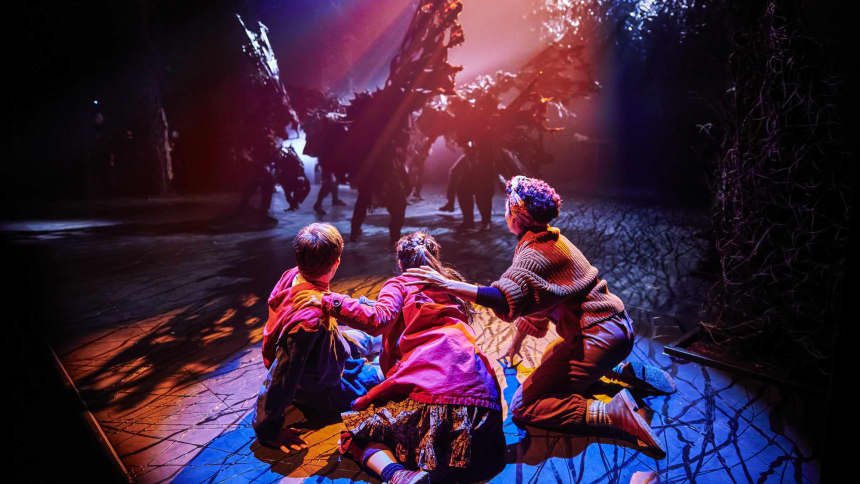 Three teenagers crouching on the floor with their back to the camera as something dark looms towards them