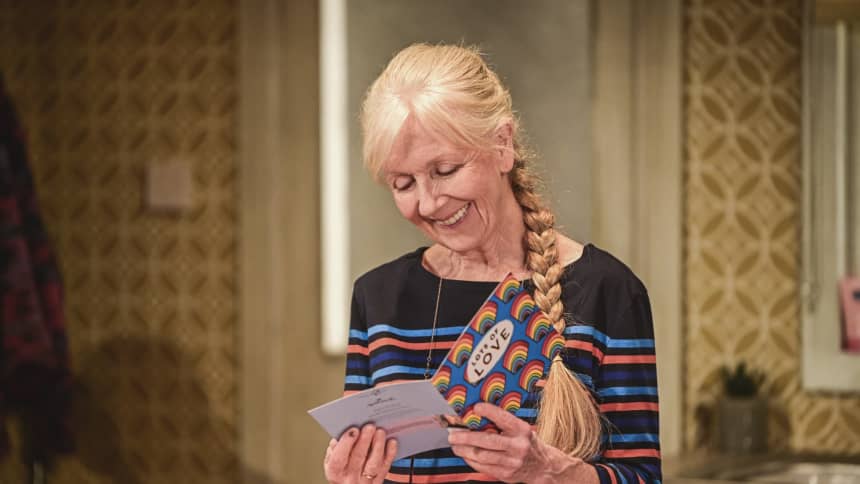 An older white woman smiling as she opens a birthday card with rainbows on the front and the words 'Lots of Love'