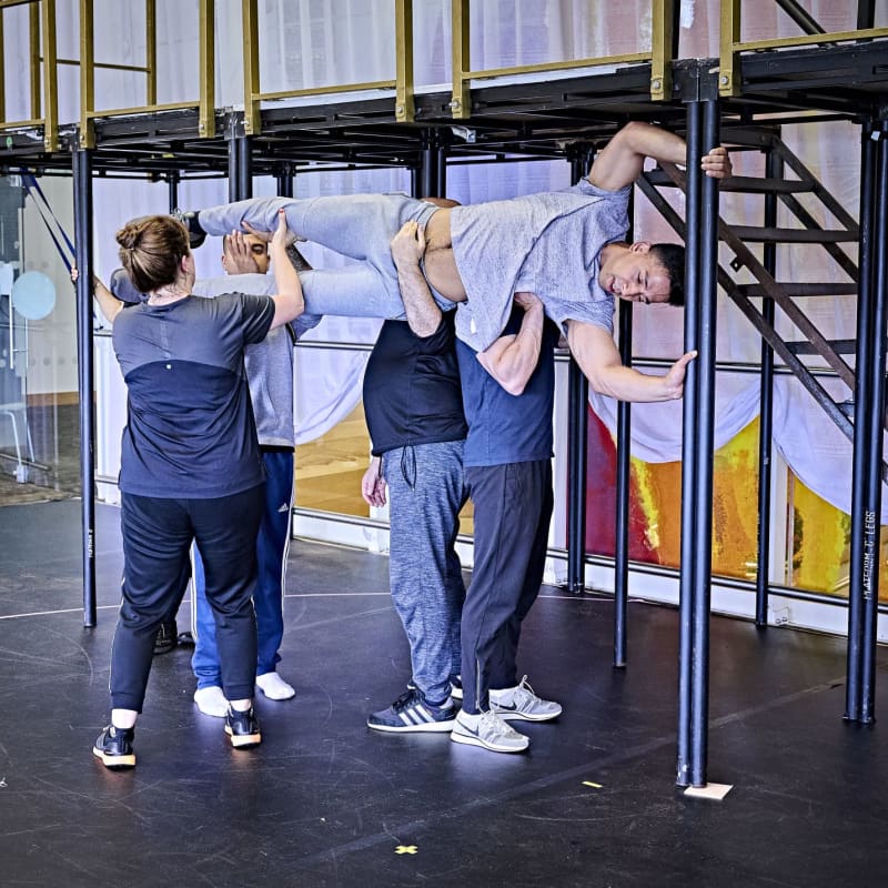 Four actors holding up another actor in the air on his side