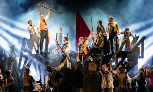 The cast of Les Misérables standing on the barricades stage set