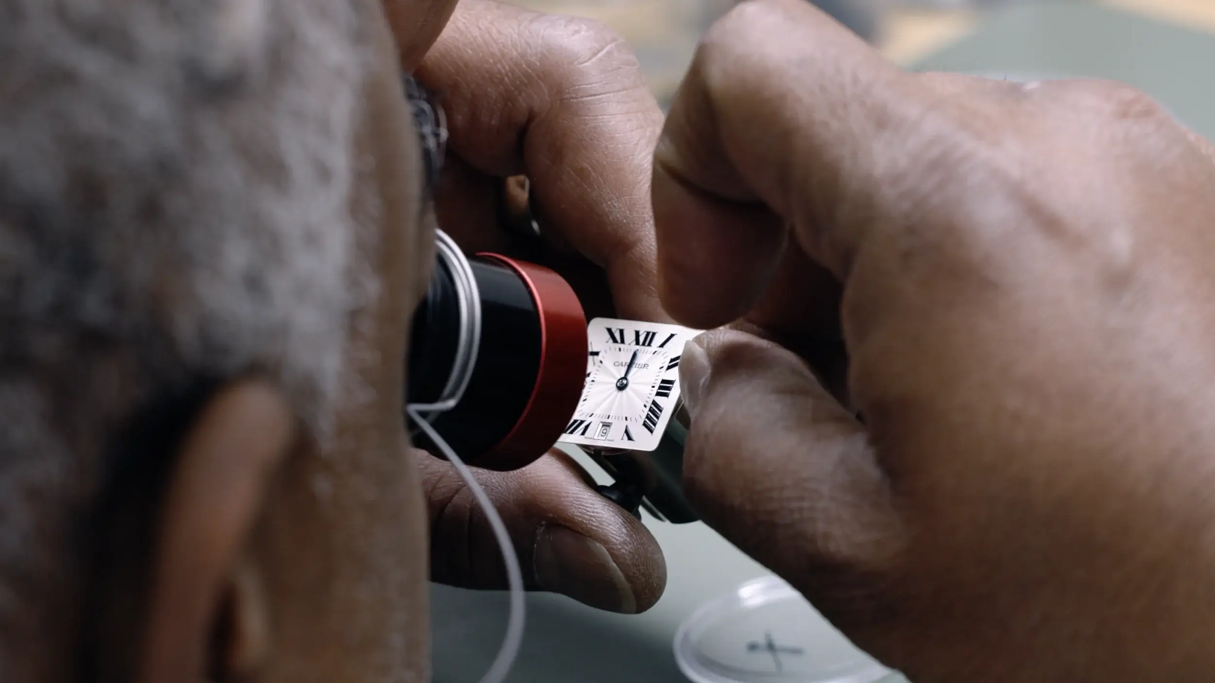 Background image of a watchmaker closely inspecting Cartier watch