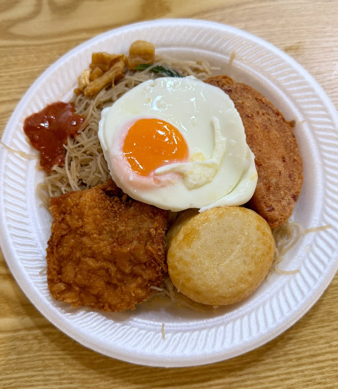 Plate of bee hoon with a fried egg, luncheon meat, fish cake, fish fillet, pork lard, little bit of chili on the side