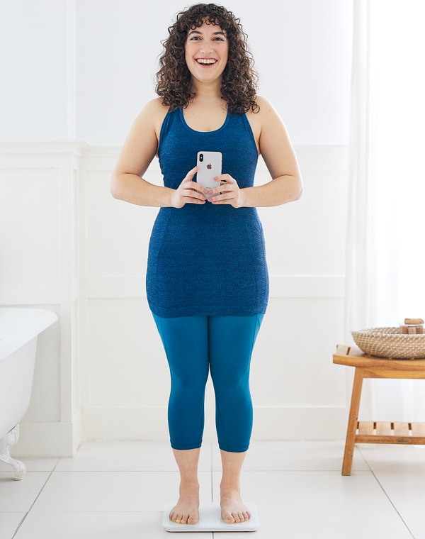 Image of women in blue clothing standing on scale taking a picture of herself.