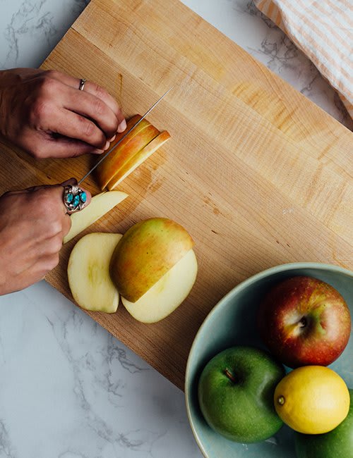 Image of a woman cutting fresh apples on wooden board.