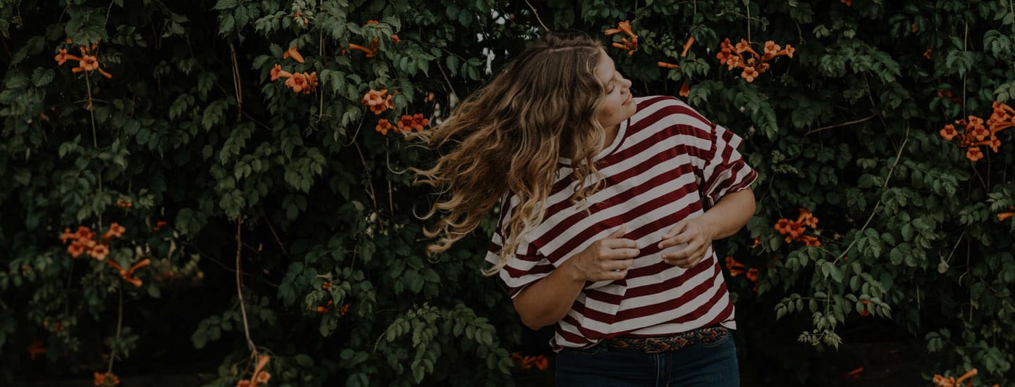 Woman standing in front of flowers flipping her hair in the wind.
