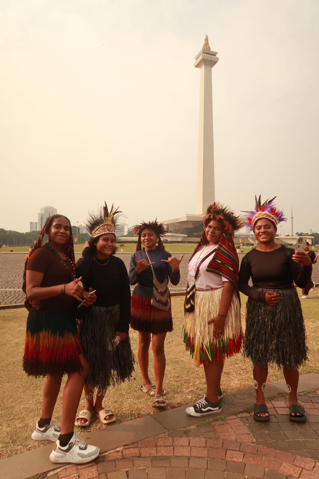 Siswi asal Papua mengenakan pakaian adat berfoto di depan Monumen Nasional
