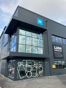 The front of the Green Hub - A black corner building with large windows. On the windows are large white outlines of product packaging