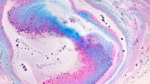 Close up of a pink, purple and blue bath bomb frothing in the water