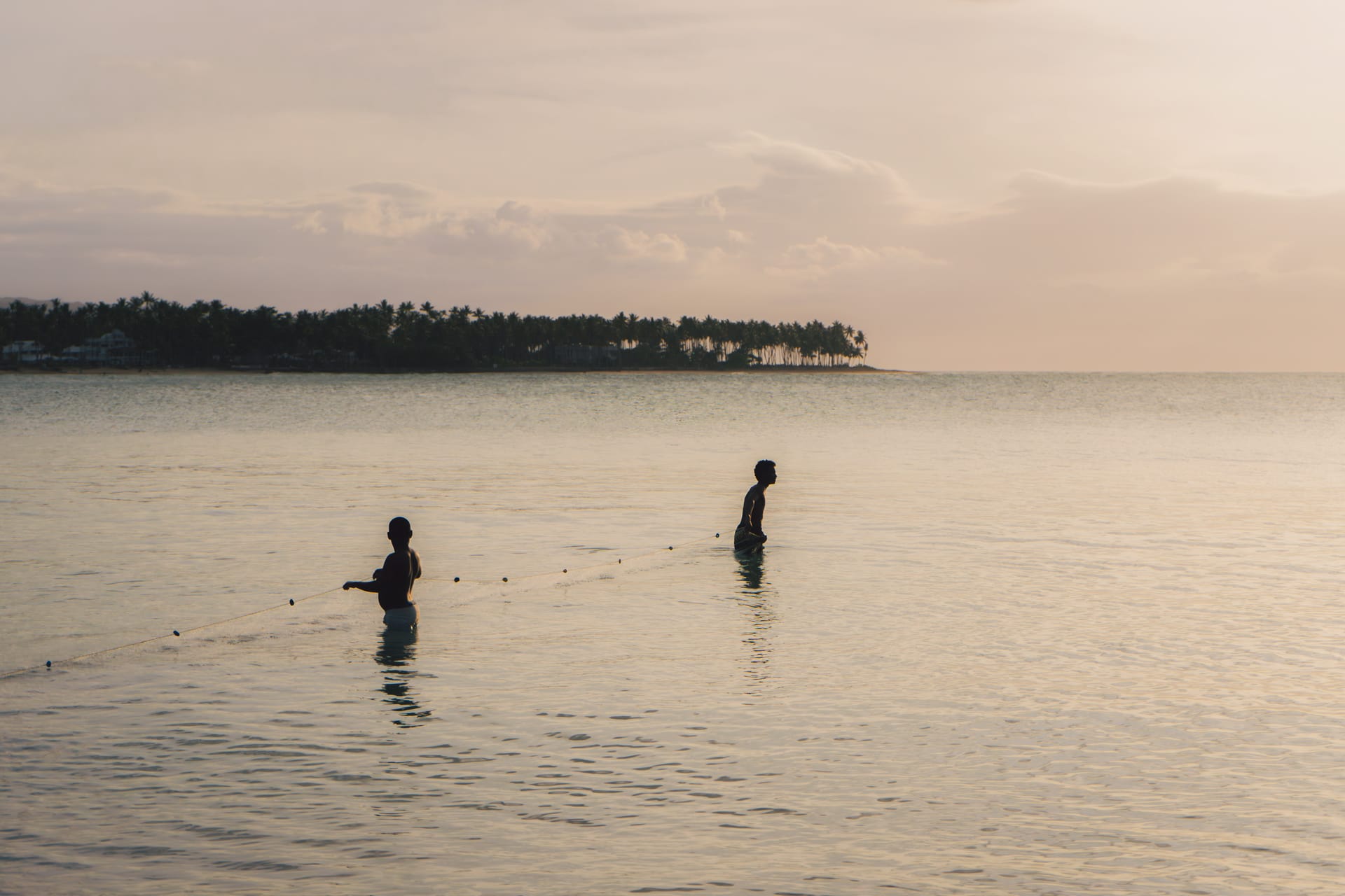 Guys throwing fishnet in the sea to fish as the sun sets
