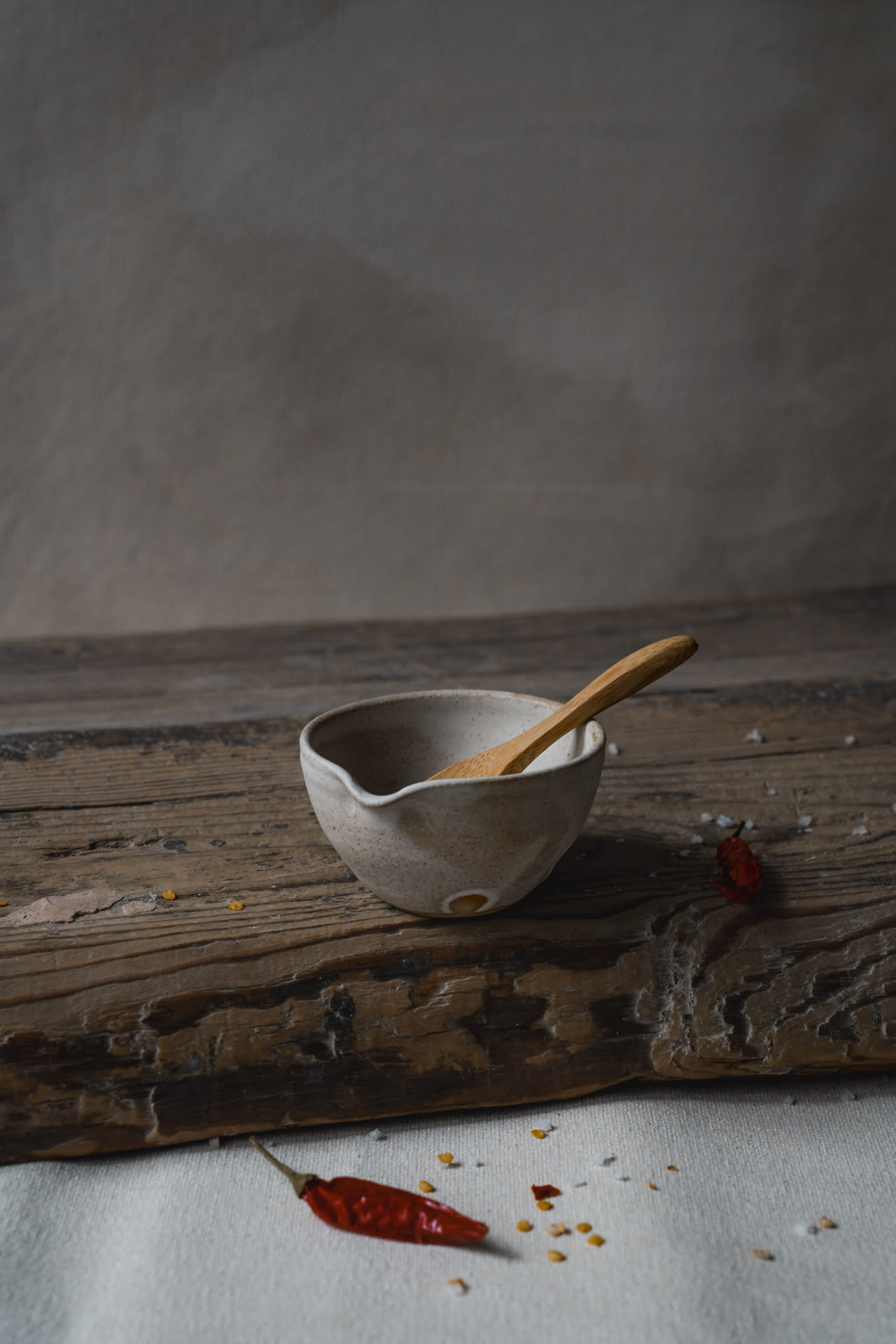 Small ceramic milk pourer and wooden tea spoon on a wooden top