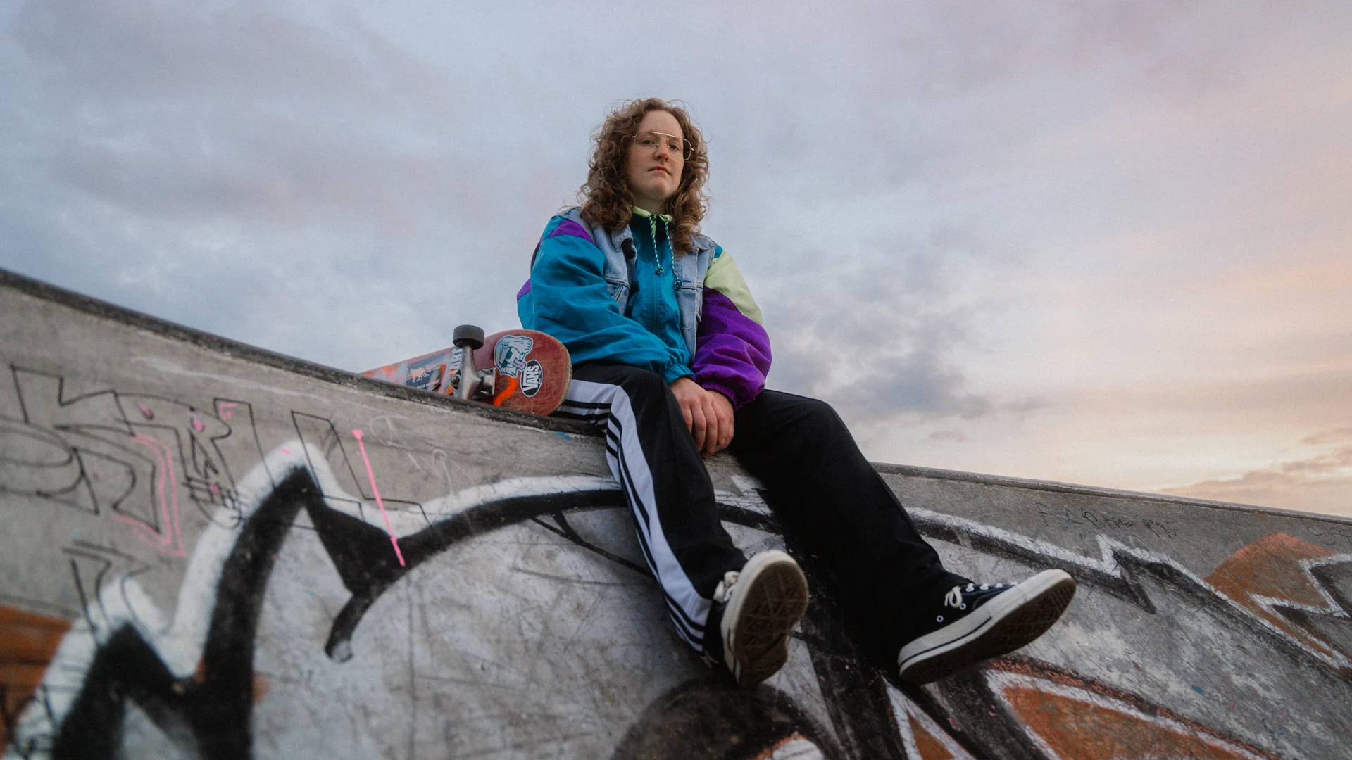 Portrait of a girl sitting on a ramp at the skate park holding her skate