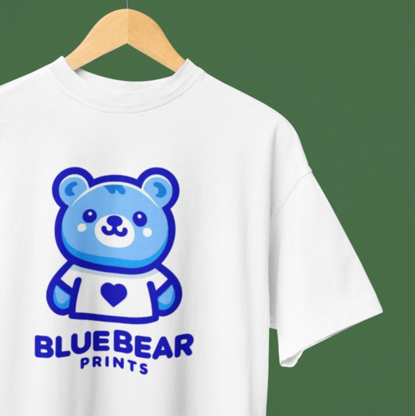 White t-shirt with Blue Bear Prints logo featuring blue bear graphic and text, custom-printed and hung on hanger against green backdrop.