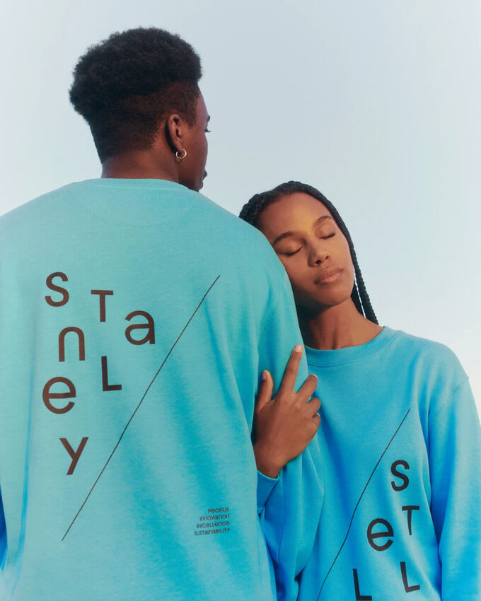 Two people wearing turquoise Stanley and Stella sweatshirts with eco slogans promoting sustainable fashion.