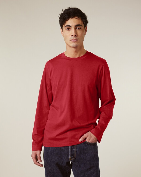 Man wearing red long-sleeve organic cotton shirt and blue jeans, promoting sustainable menswear on neutral background.