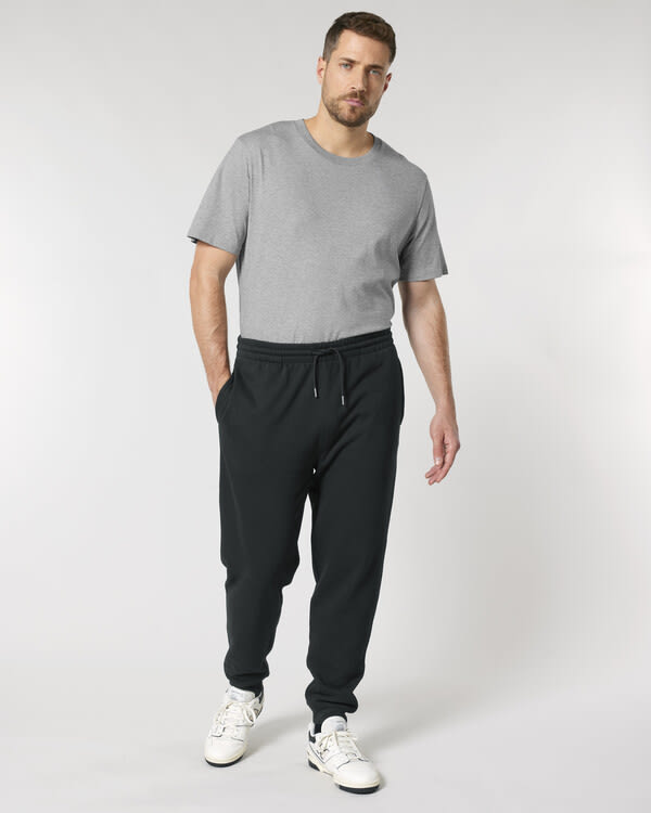 Man wearing grey organic cotton t-shirt and black jogger pants with white trainers, showcasing casual sustainable fashion.