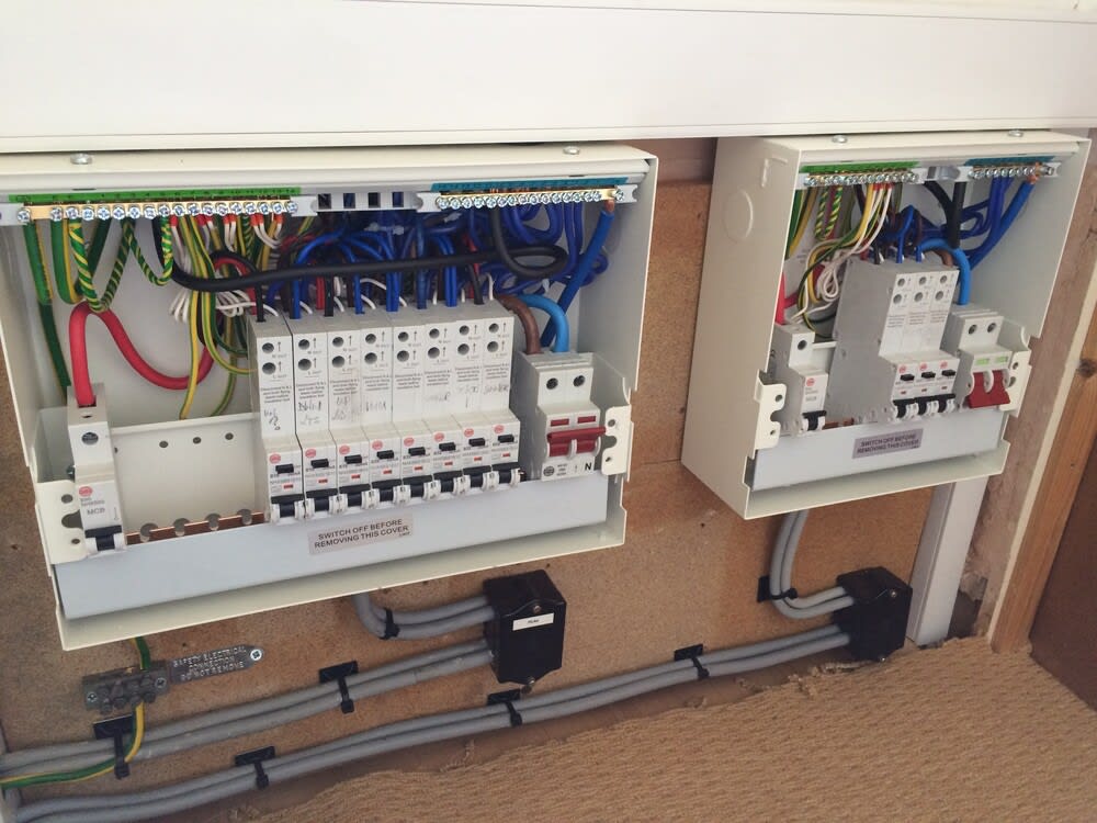 Electrician installing a modern consumer unit in a UK home with labeled circuit breakers and safety gear