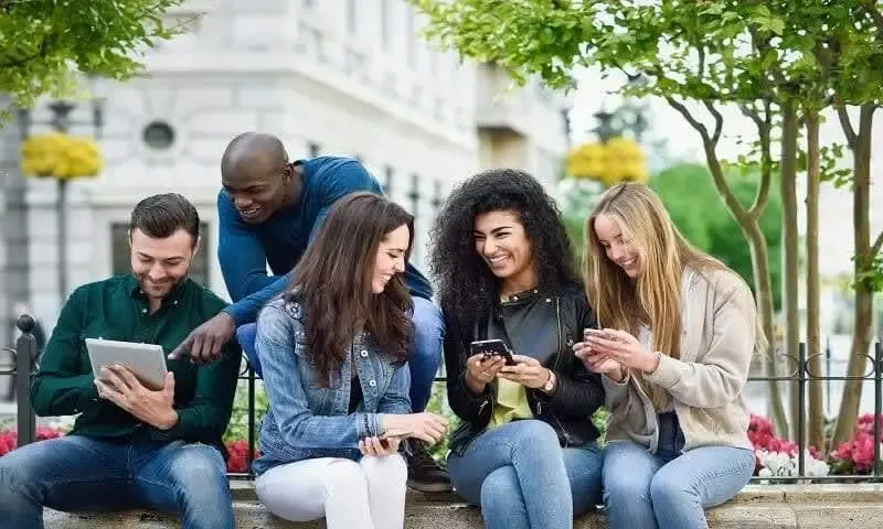 Grupo de 5 pessoas, dois homens usando tablets e três mulheres mexendo no celular, todos sorrindo. A imagem representa uma discussão animada sobre o que é SEO.