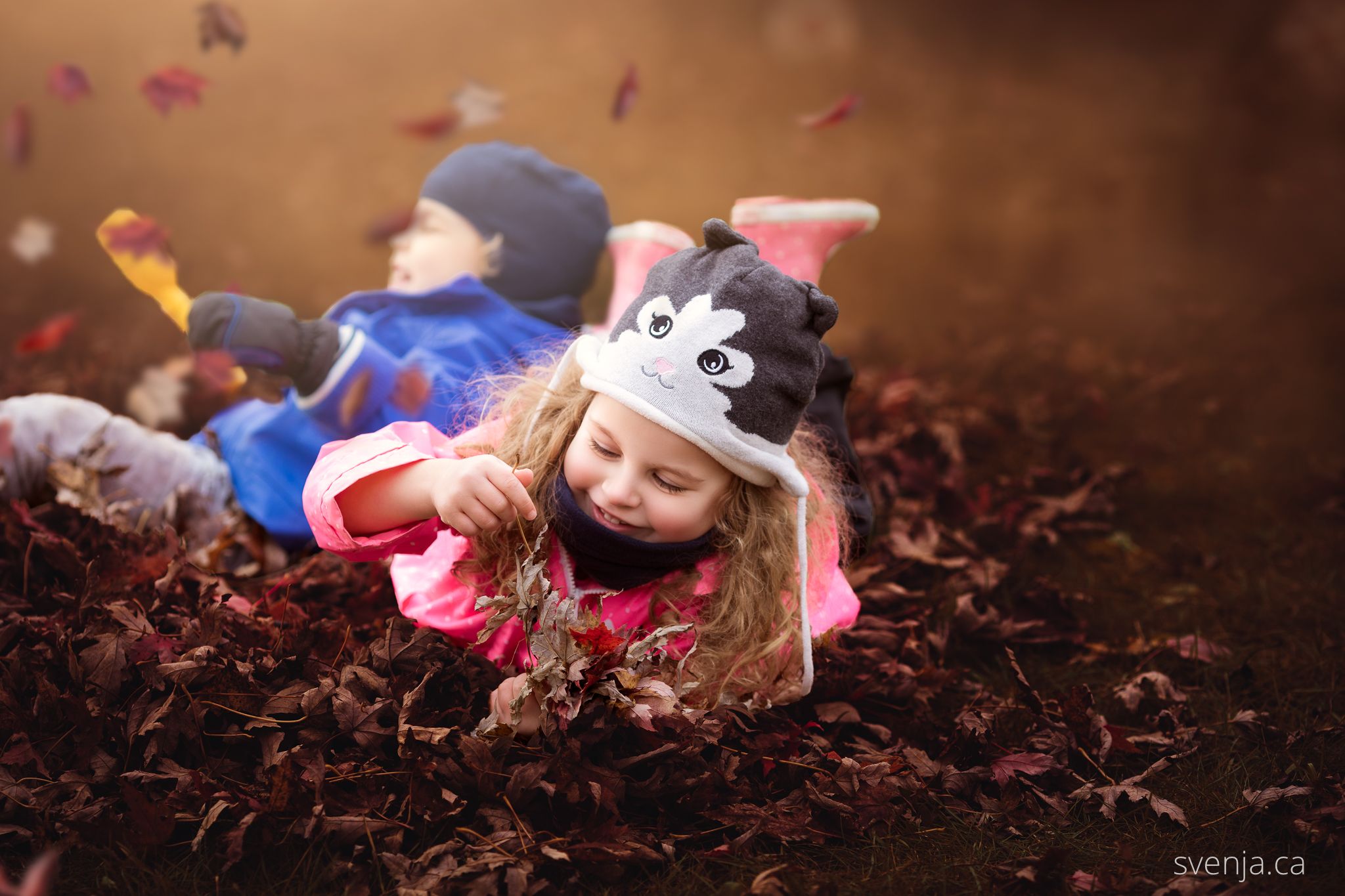 two young children playing with leaves in autumn