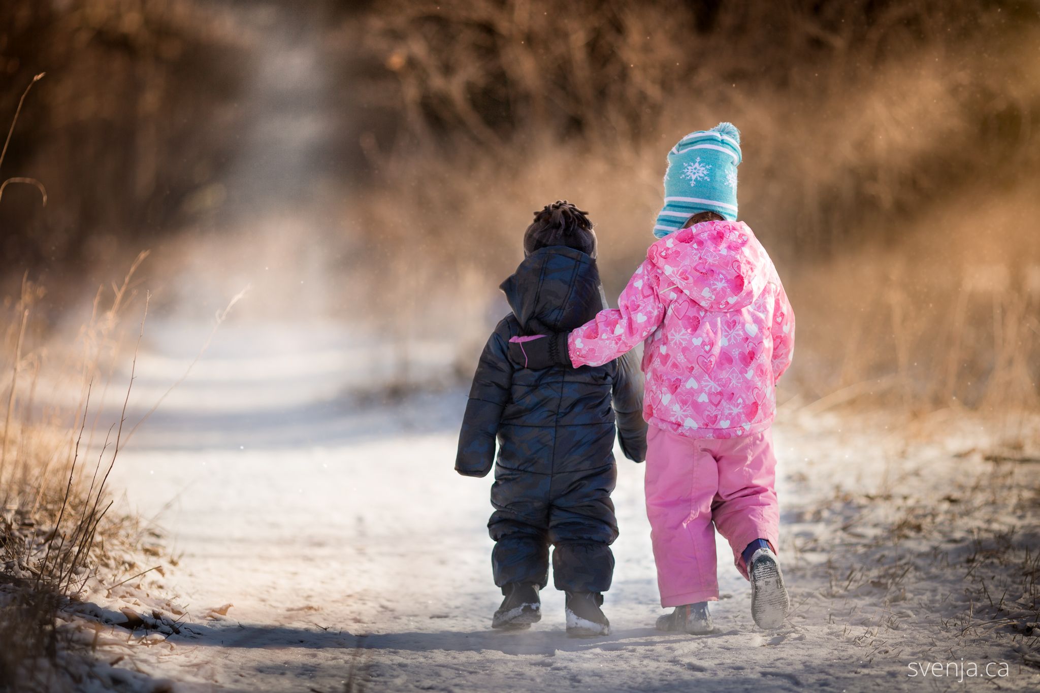 boy and girl in snowsuits walk down a path