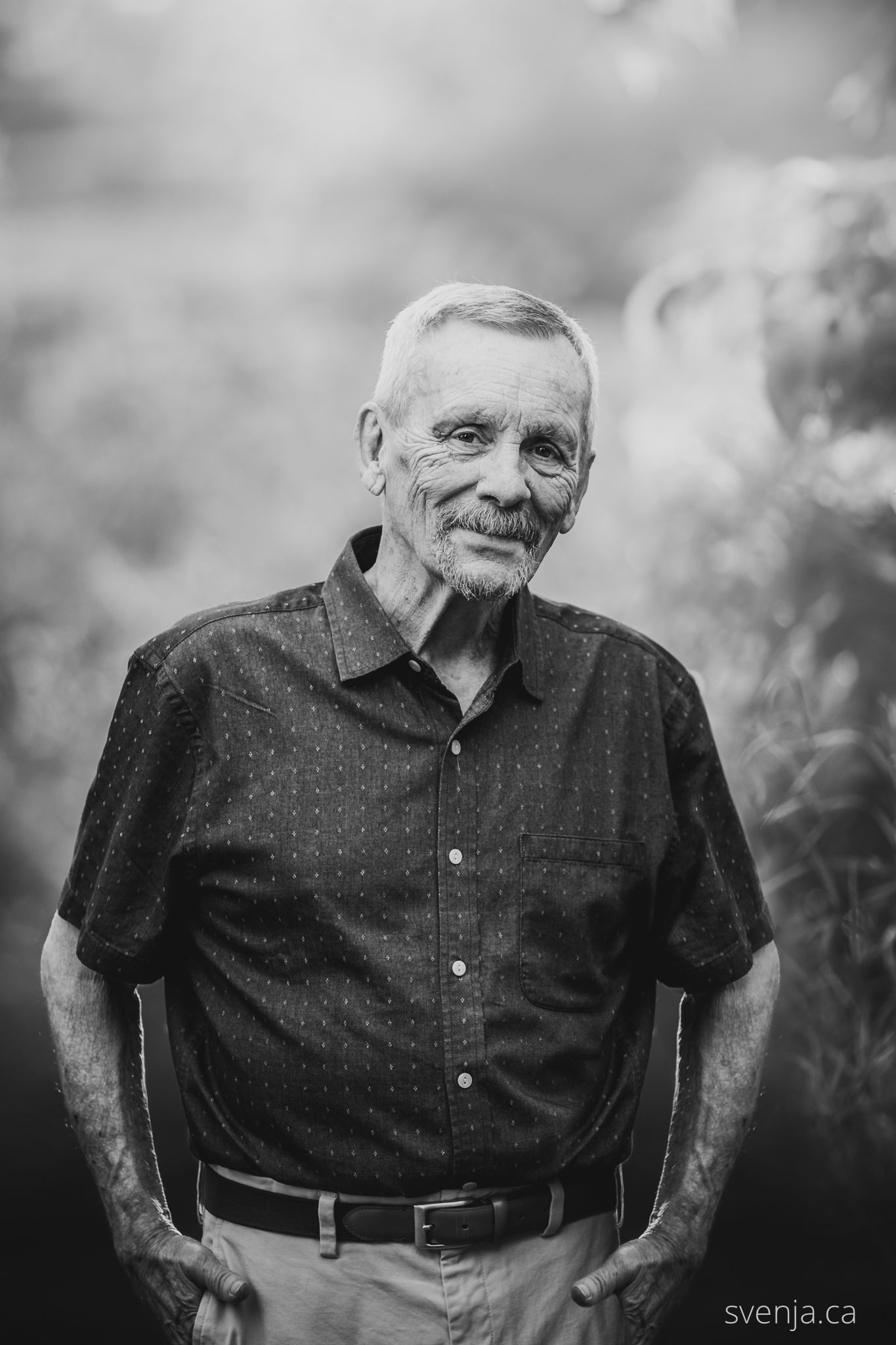 black and white photo of white-haired man with hands in his pockets