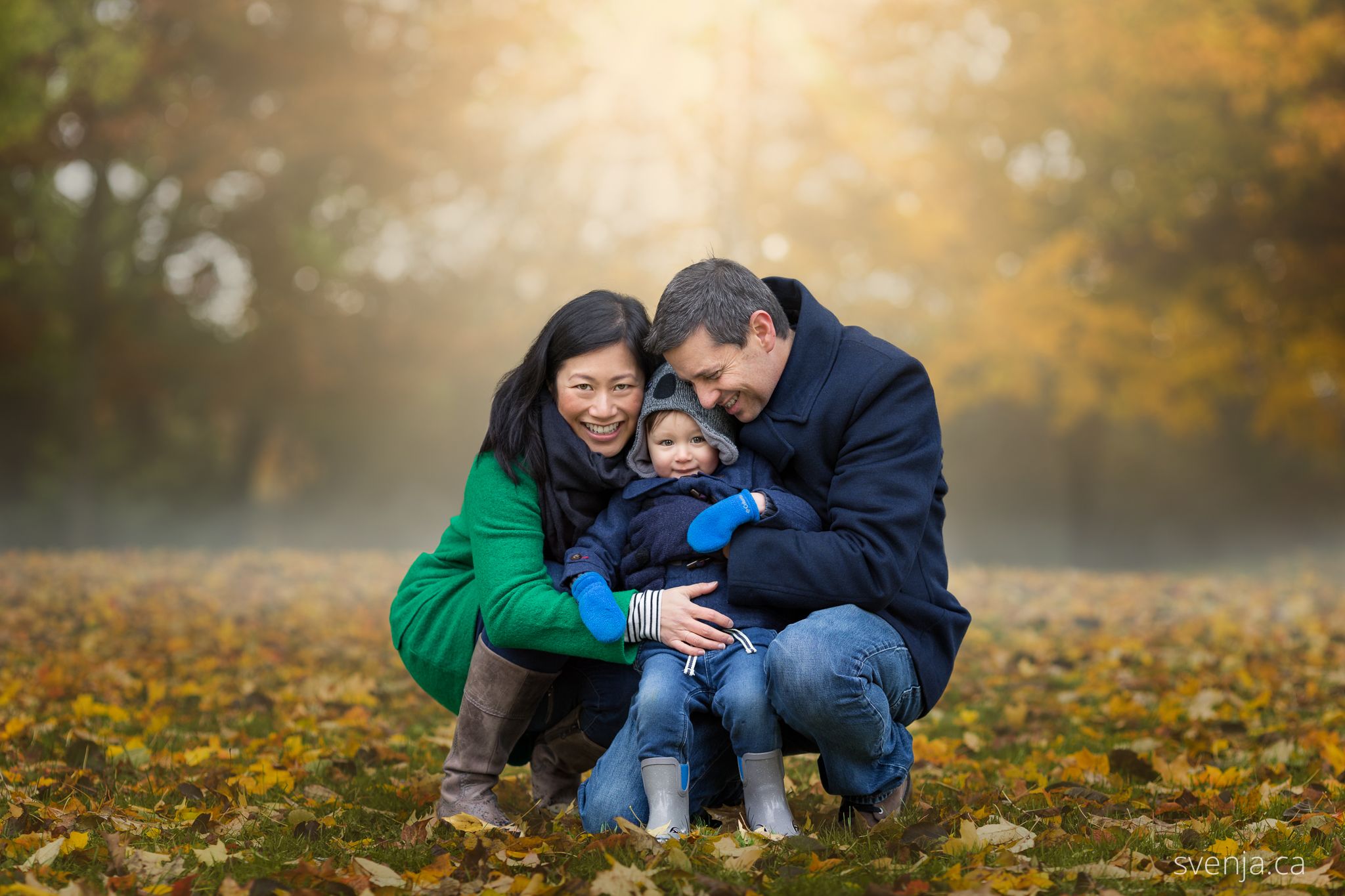 father and mother hold their child in the sunlight on a fall day