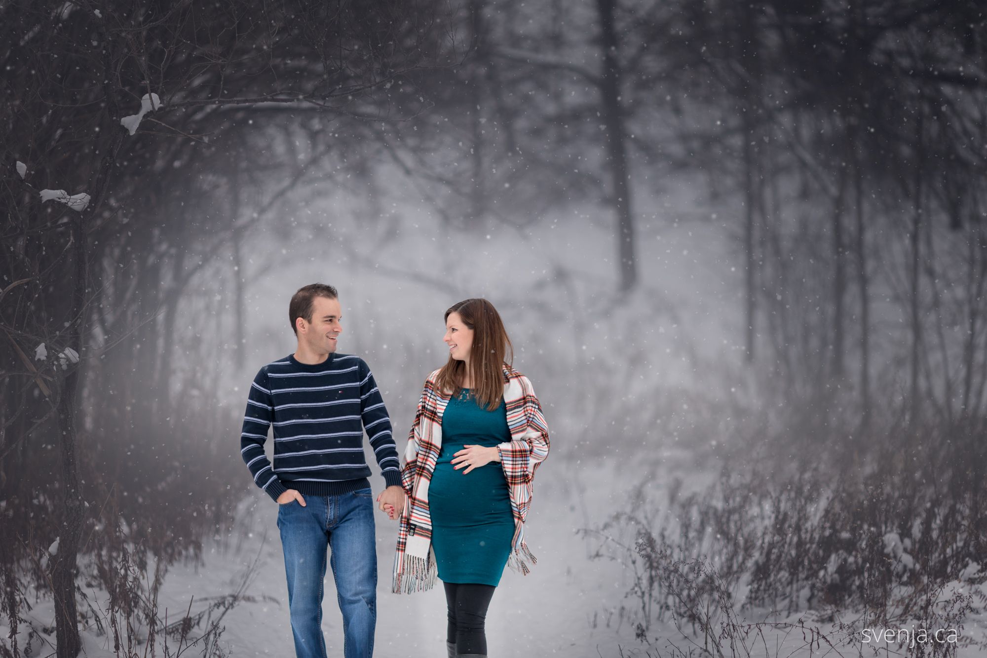 an expecting couple walked together through a snowy forest