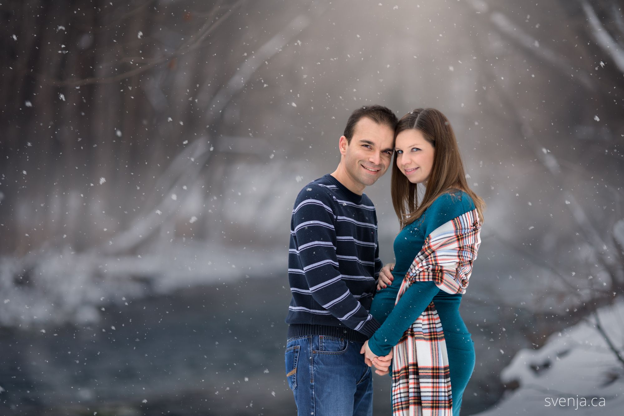 expecting mother and her husband embrace closely with a snowy background