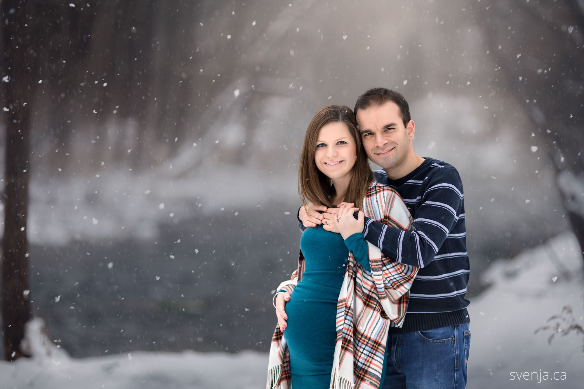 expecting mother and her husband embrace closely with a snowy background